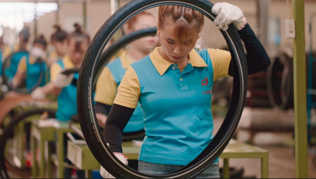 Arbeiterin in blauem Tshirt überprüft einen Schwalbebreifen in der Werkhalle, Vietnam